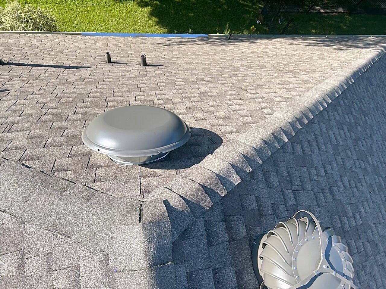 A powered attic vent and a turbine set into a finished shingle roof