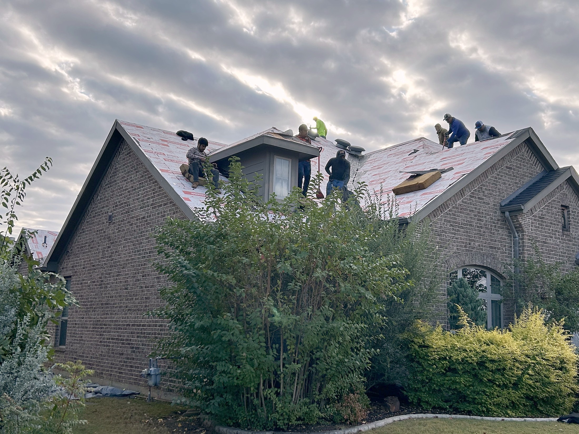 A crew laying underlayment across a brick house at first light