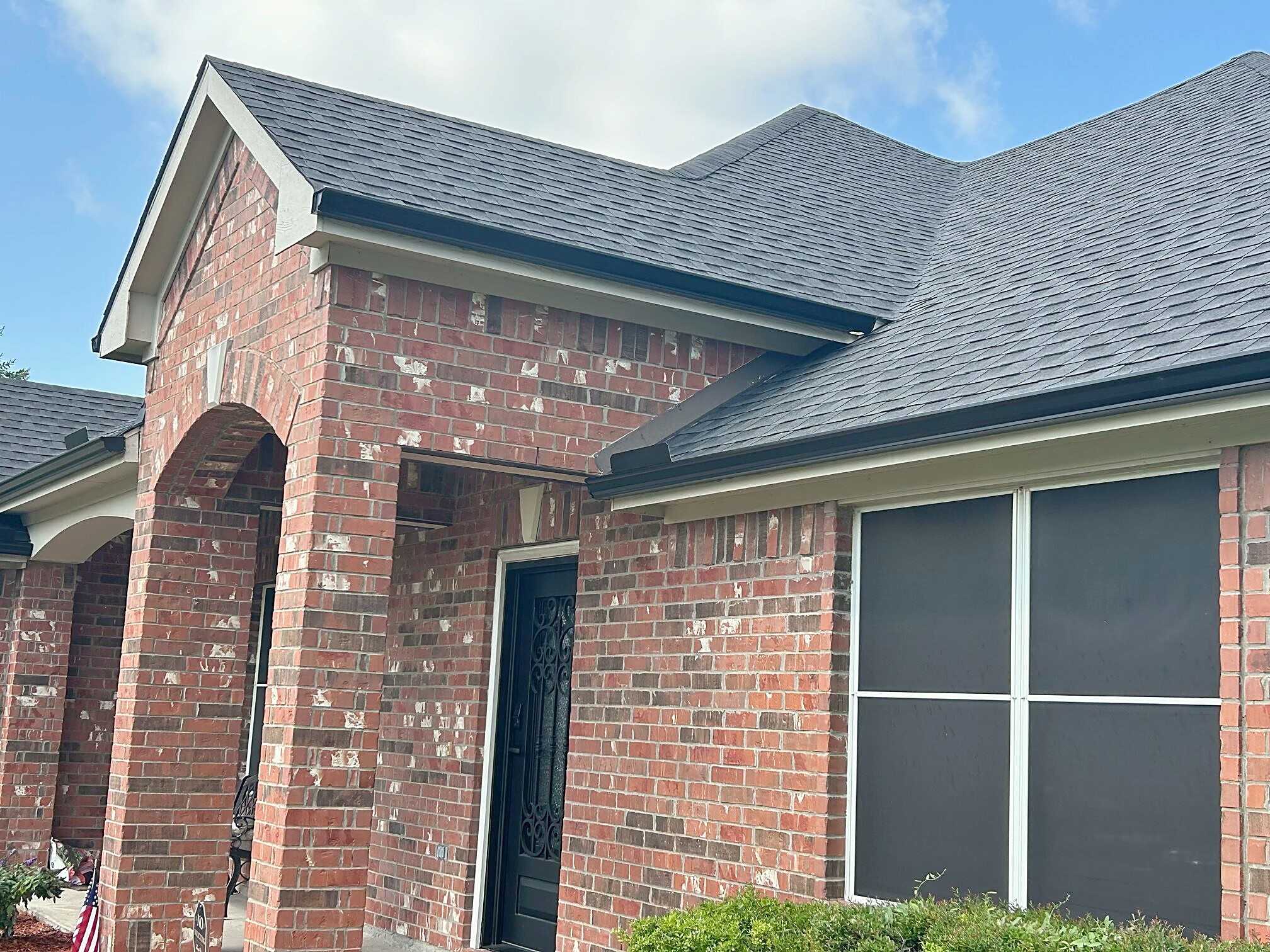 A finished charcoal shingle roof over the brick gable and arched entry of a Texas home