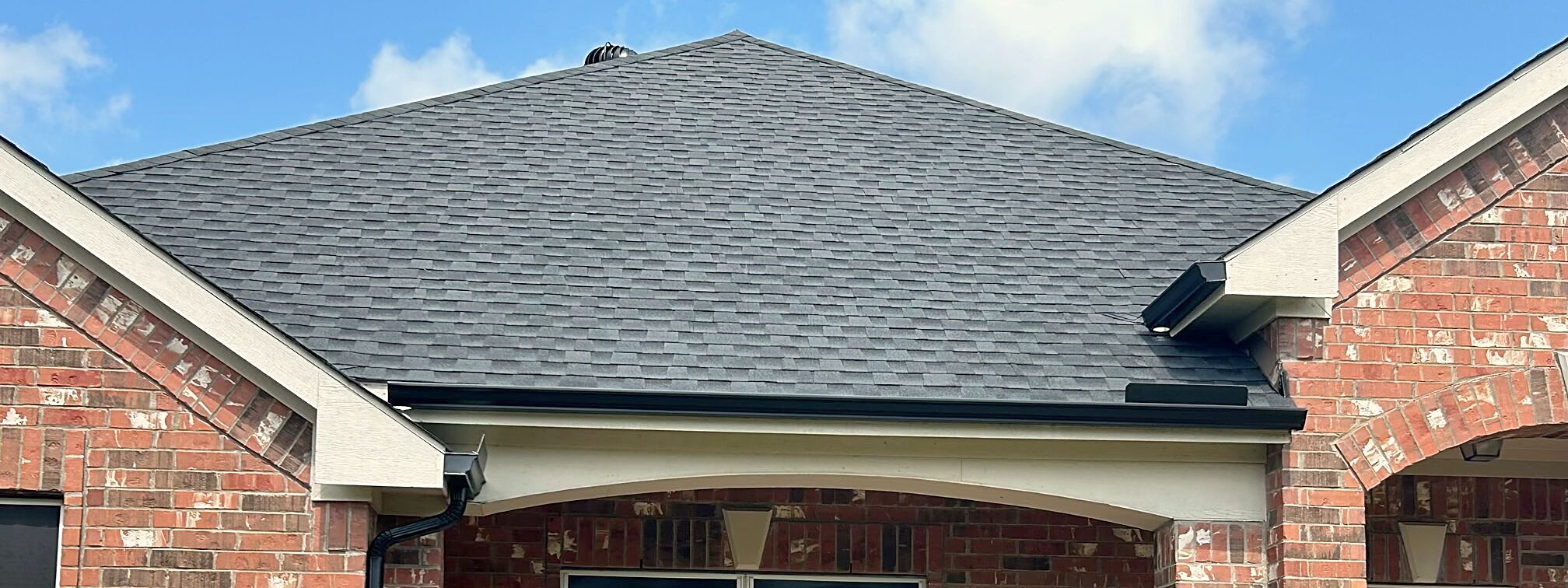 A finished charcoal shingle roof and new gutter over the arched brick porch of a Texas home