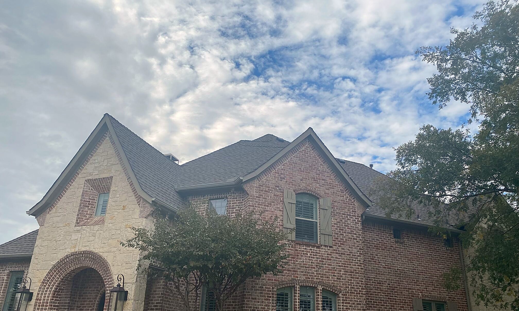 A new charcoal shingle roof over the steep gables of a brick and stone two-story home