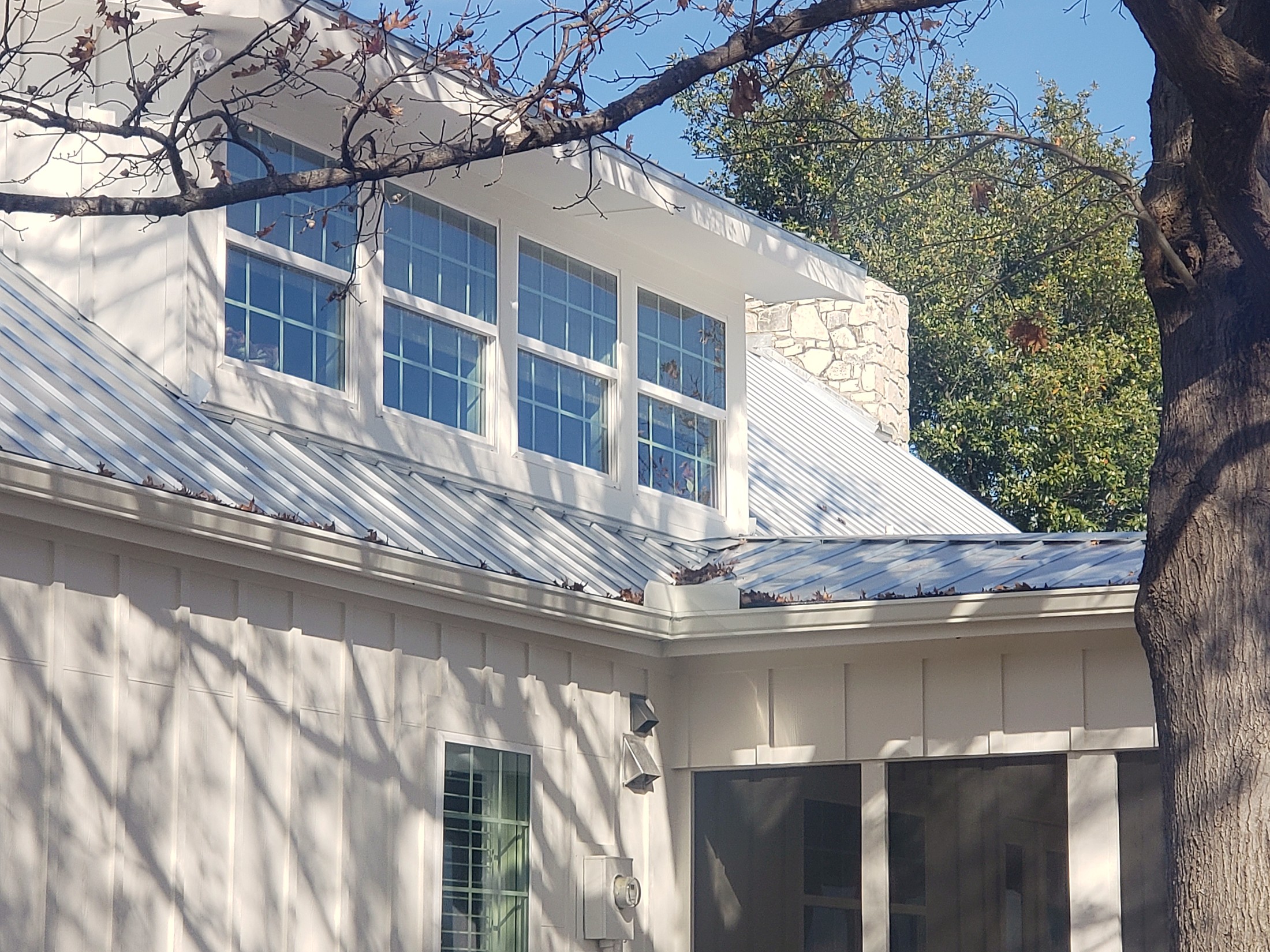 A standing seam metal roof running up to a white dormer and a stone chimney