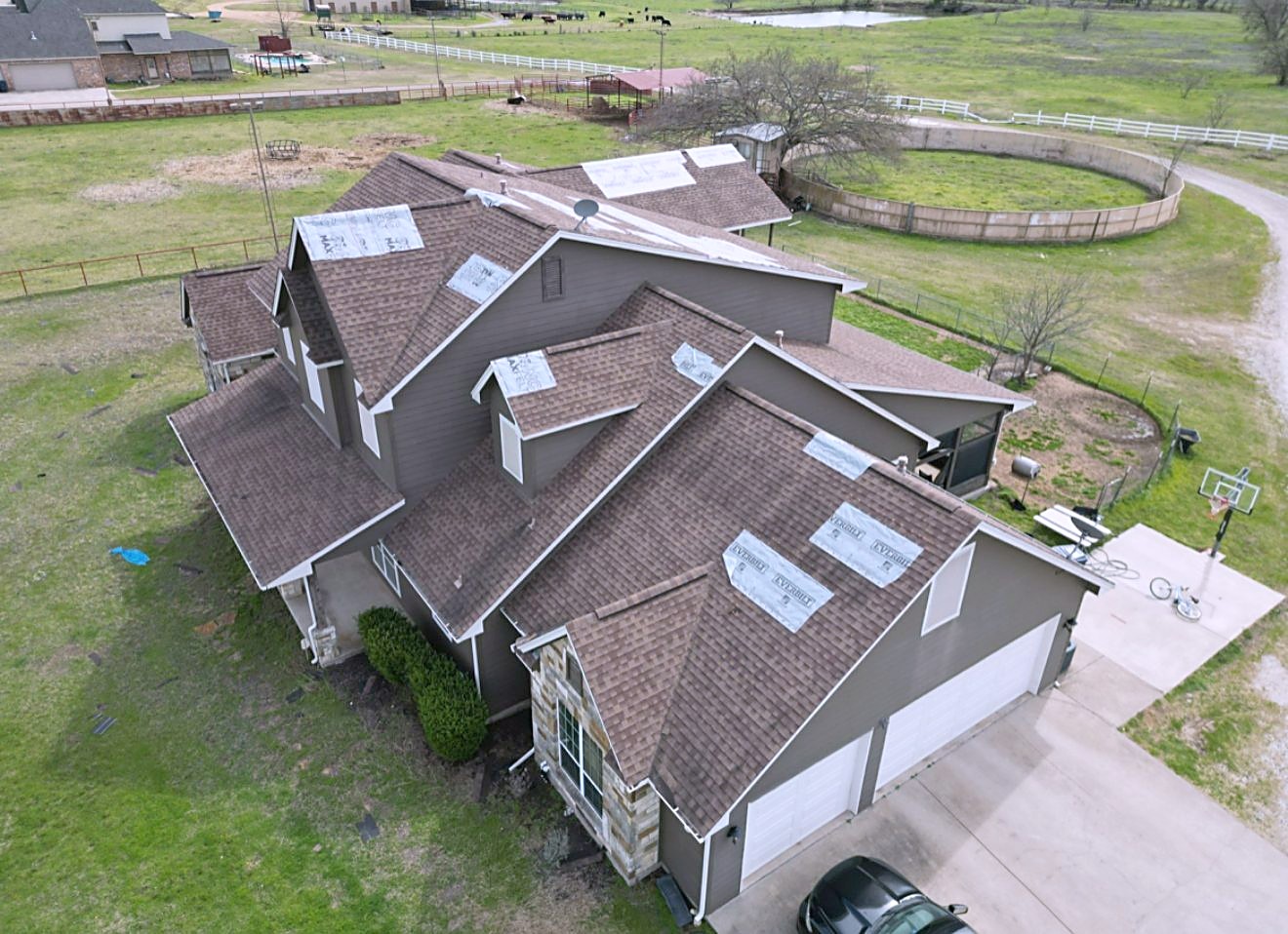 Aerial view of a new brown shingle roof on a large country home with pasture and a barn behind it