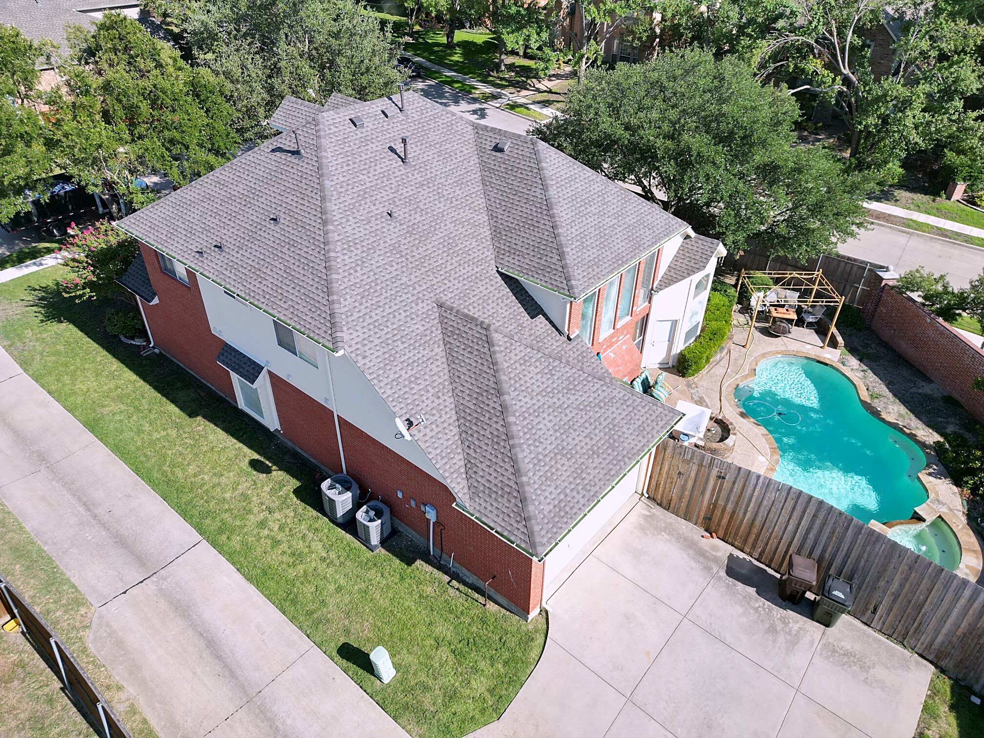 Aerial view of a weathered-wood shingle roof on a two-story brick home with a pool in the back yard