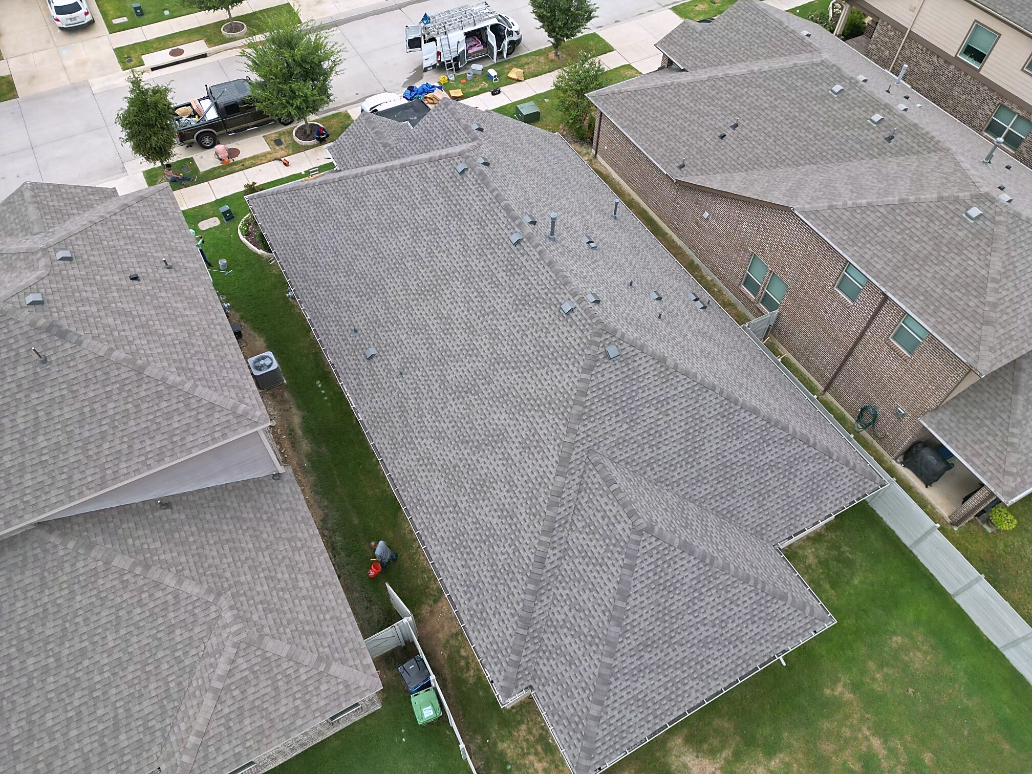 Aerial view of three finished shingle roofs along a North Texas street with a work van at the curb