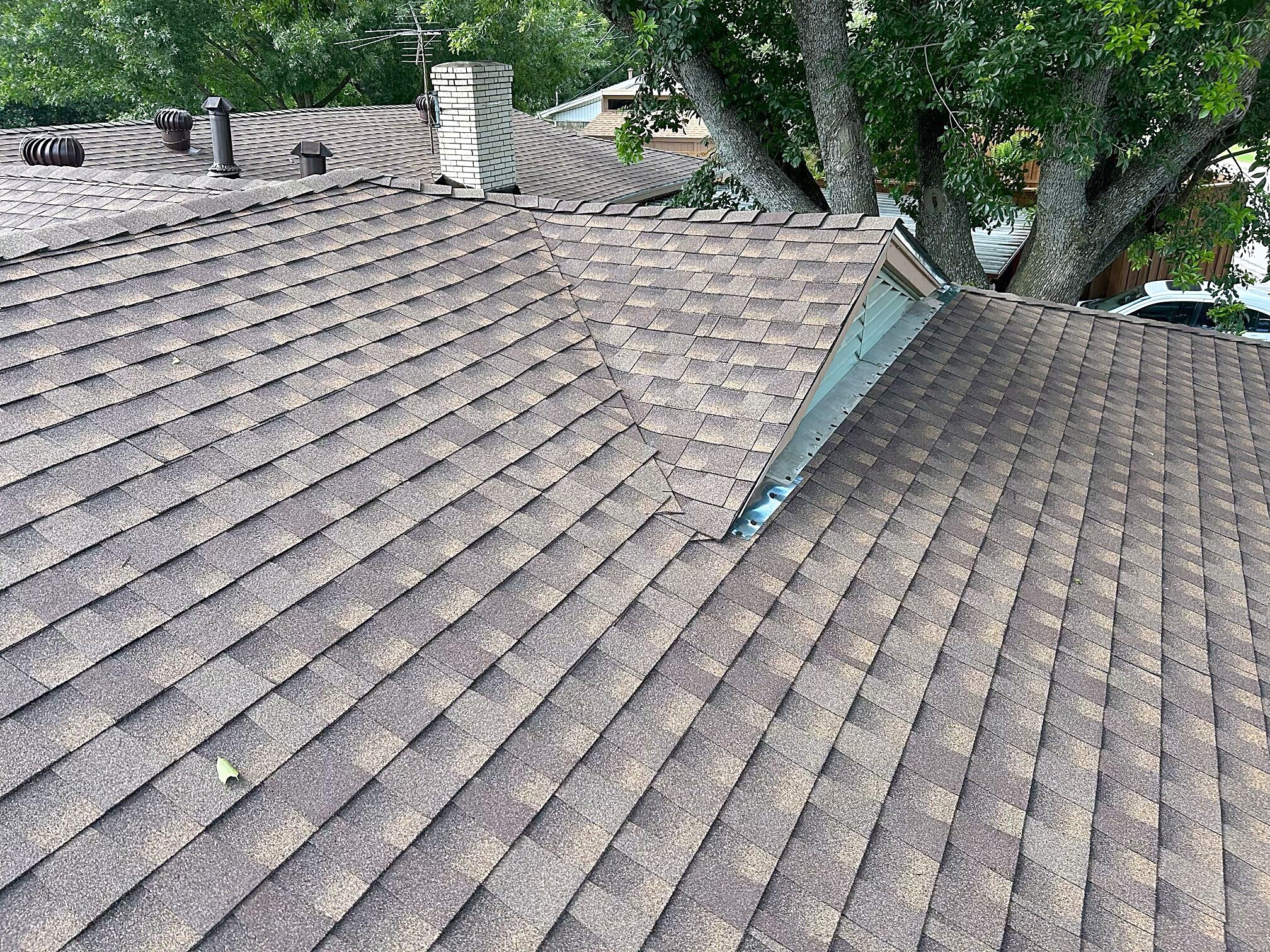 A finished weathered-wood shingle roof with ridge cap, turbine vents and a brick chimney