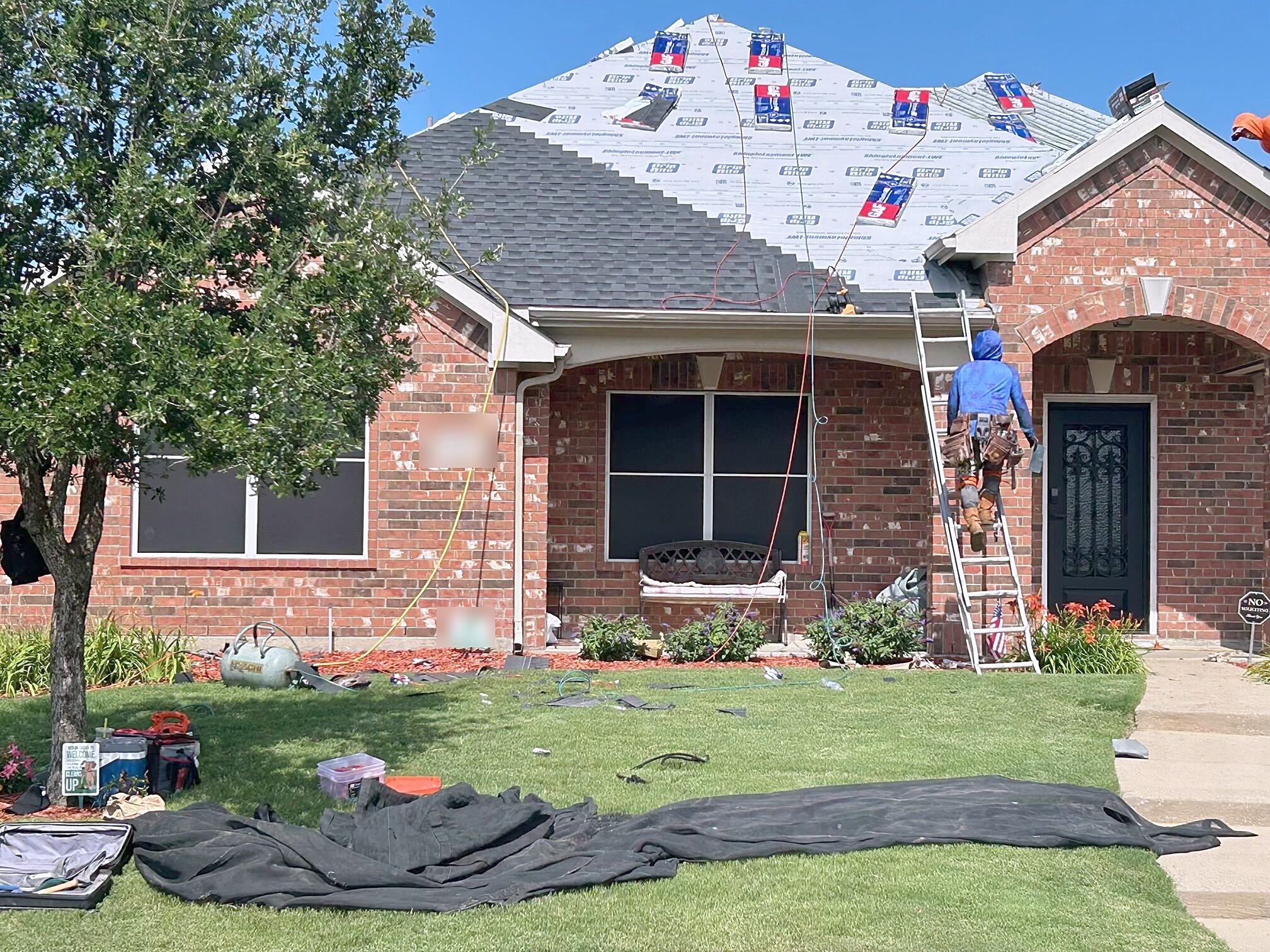 A roof half stripped to underlayment with shingle bundles stacked on the slope and a roofer on the ladder