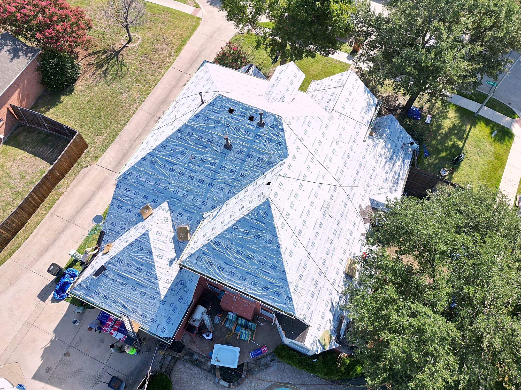 Aerial view of a house fully covered in synthetic underlayment with shingle bundles stacked in the driveway