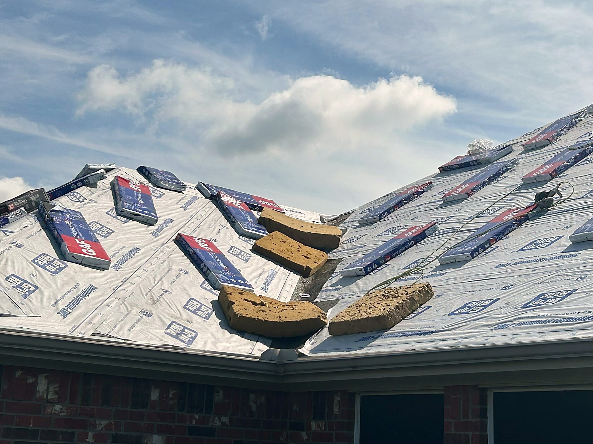 Shingle bundles laid out across fresh synthetic underlayment on a hip roof